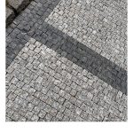 Hellgraue Pflastersteine werden durchzogen mit breiten Linien von dunkleren Pflastersteinen.