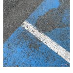 Blaue und weiße, teilweise abgefahrene Farbe einer Parkplatz Makierung auf Asphalt. Das Bild ist schräg so dass die weiße Begrenzungslinie in die rechte untere Ecke zeigt.